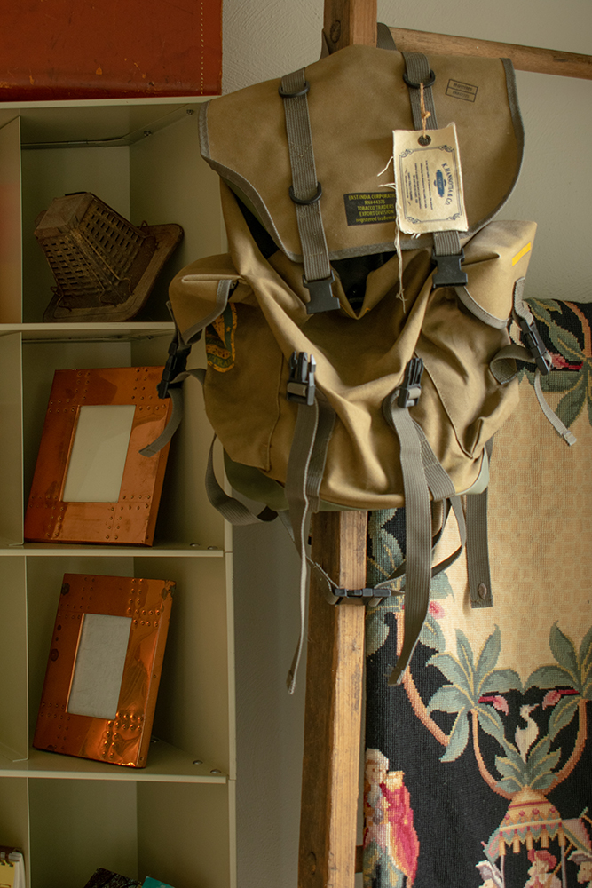 Bookbag with canvas tag hanging on textile ladder in front of shelf with photo frames. Product photography for Relic Vintage.