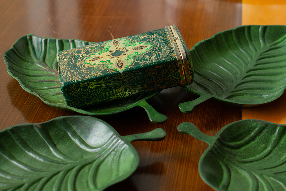 Green decorative vintage matchbox sitting on leaf-shaped ashtrays. Product photography for Relic Vintage.
